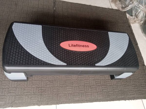 A gray and black aerobic step board with a textured surface. The board has a rectangular shape with rounded corners and four non-slip feet. The word "Litefitness" is printed on the top of the board in red.