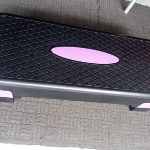 A black aerobic step board with a pink oval in the center. The board has a textured surface and raised edges for stability.