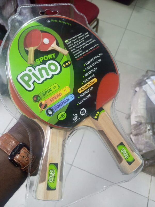 A pair of red and black table tennis paddles in a plastic blister pack. The paddles have wooden handles and rubber surfaces. The packaging includes the brand name "Pino" and information about the product's specifications and recommended age.