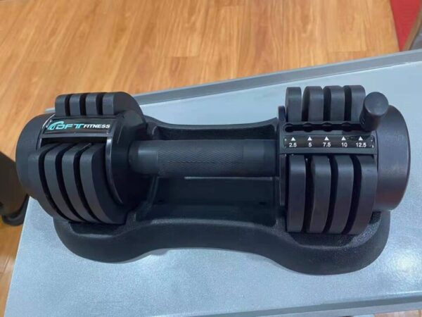 A black adjustable dumbbell with the brand "BFIT FITNESS" printed on it. The dumbbell has a digital display that shows the weight setting, which ranges from 2.5 to 12.5 kilograms. The dumbbell also has a handle and a base for storing the weights.